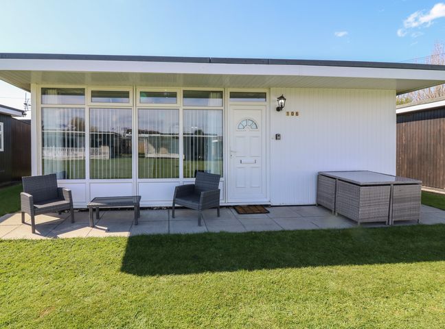 A white exterior house with patio chairs a table and a green lawn at 106 Cherry Park Chapel St Leonards