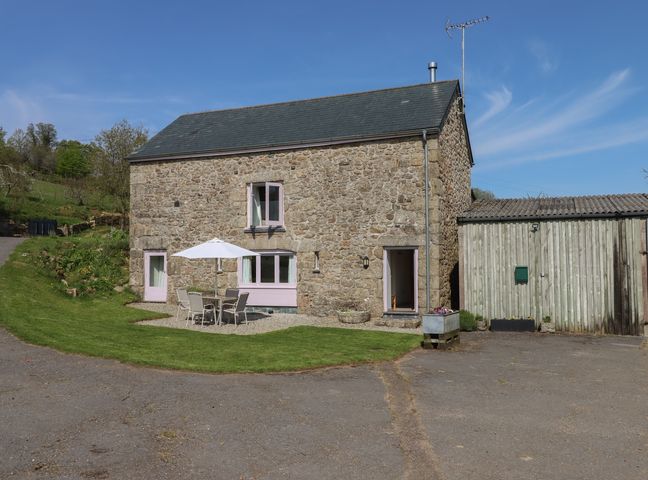 A stone building with a patio table and chairs under an umbrella and an adjacent wooden shed at Puddaven Barn in North Bovey near Chagford