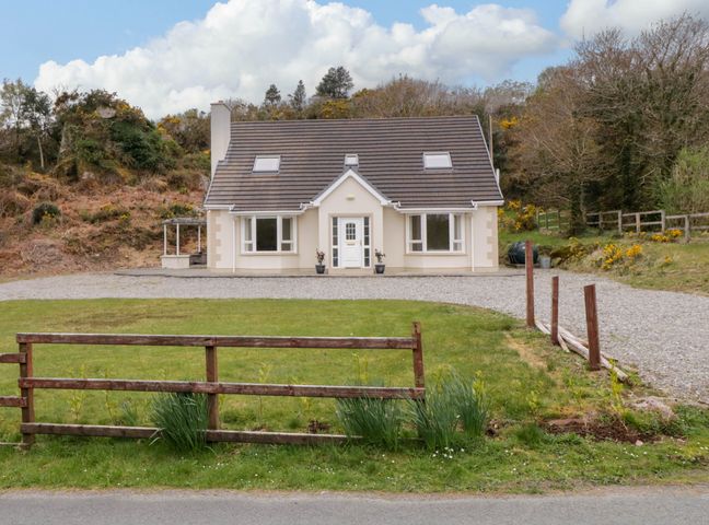 A detached house with a front lawn gravel driveway and wooden fence near a wooded area at Riverside Cottage near Crolly