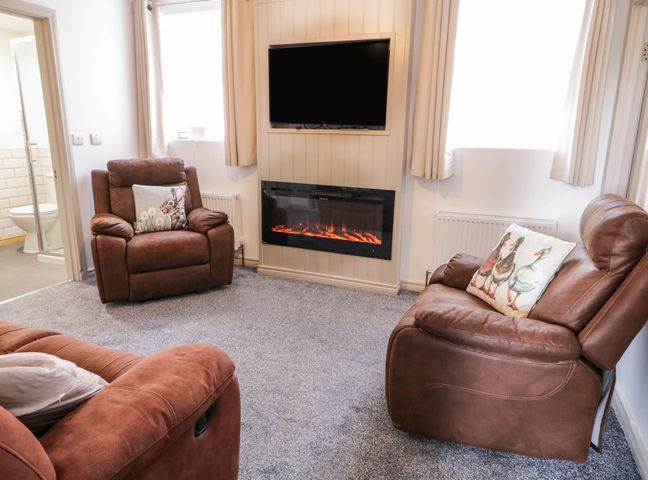 A living room with brown armchairs and a wall mounted TV above an electric fireplace at Gola View in Magheraclogher near Derrybeg