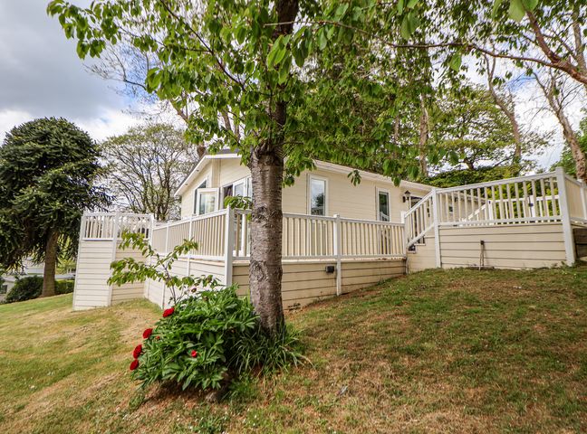 A house with a white fence and open windows on a grassy slope with trees and flowers at 155 Woodland Hall Lyons in Ruthin