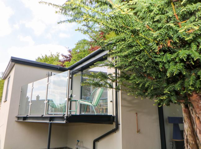 An outdoor glass balcony with two green chairs and a small table next to a cream building with a tree nearby at Yew Tree Cottage in Matlock