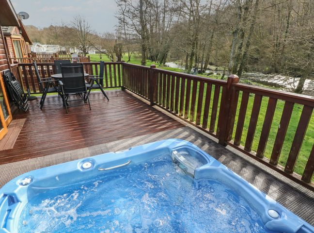 A hot tub on a deck with chairs and table at Riverside Lodge 3