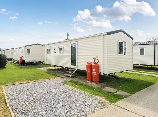 A row of static caravans with propane gas cylinders outside on a grassy area at Golden Dune - Hayling Island in Hayling Island Holiday Park