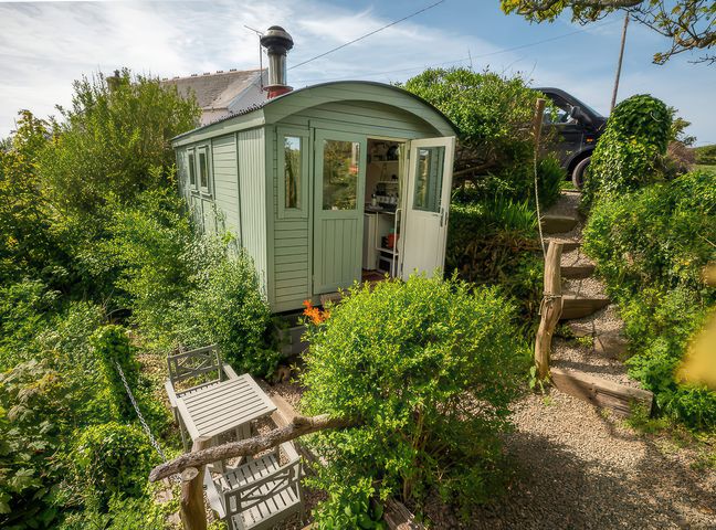 A hut surrounded by greenery with steps leading to a driveway at The Shepherd Hut near Nine Wells near Solva
