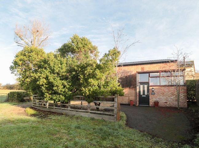 An exterior view of a house surrounded by trees and a fence at Wellinghill Cottage at Wellinghill House Charlton Kings