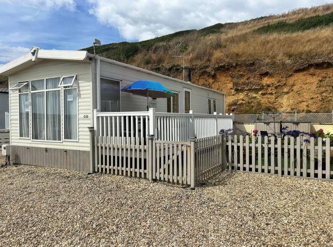 A mobile home with a deck and fence at Freshwater Beach Holiday Park - Holiday Accommodation 17116 in Burton Bradstock near Bridport