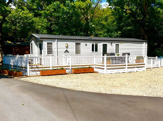 A mobile home with a deck and planters at Aberdunant Hall Holiday Park - Holiday Accommodation 21962 in Prenteg