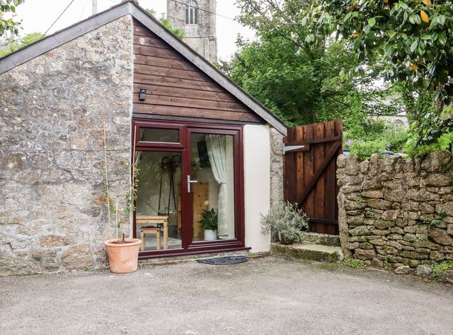 An exterior view of a small building with a door and window at Lannlyvri Lodge in Lanlivery near Lostwithiel