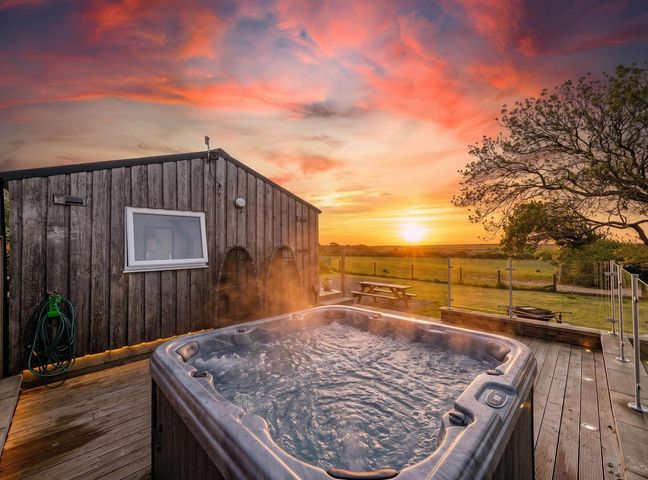 A hot tub next to a wooden building during sunset at The lodge at Plumstone View in Letterston