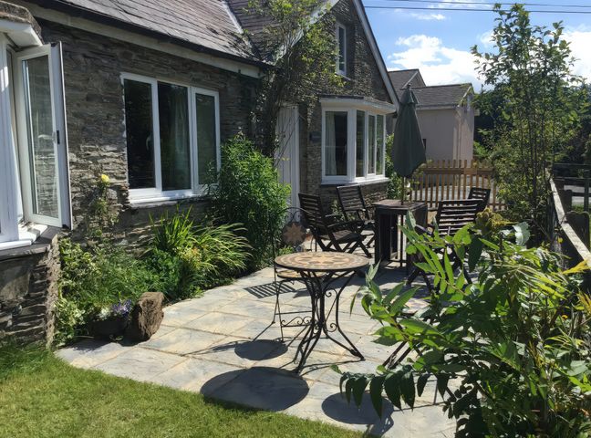 A garden with stone wall, table, chairs and plants at Glanyrafon Smithy in New Quay