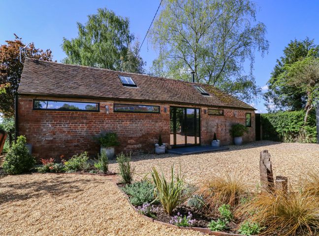 An exterior view of a brick building with surrounding plants and gravel at The Barn