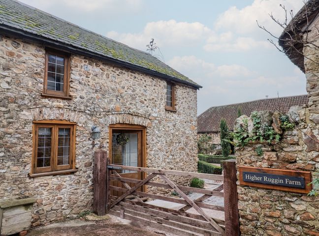 An exterior view of Higher Ruggin Farm in Wellington with stone walls and a wooden gate