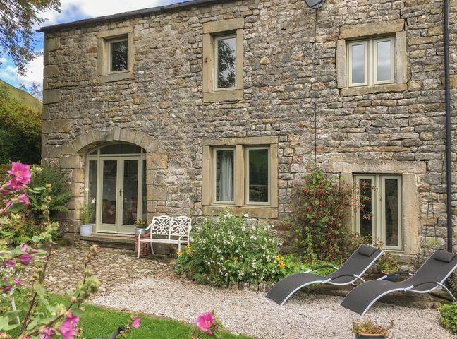 A stone cottage with windows and lounge chairs in the garden at Litton Hall Barn Cottage Skipton