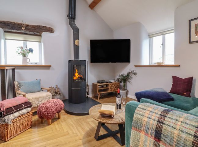 A living room with a wood burning stove and seating area at The Old Cartshed | Yr Hen Gwt Cart in Abergele