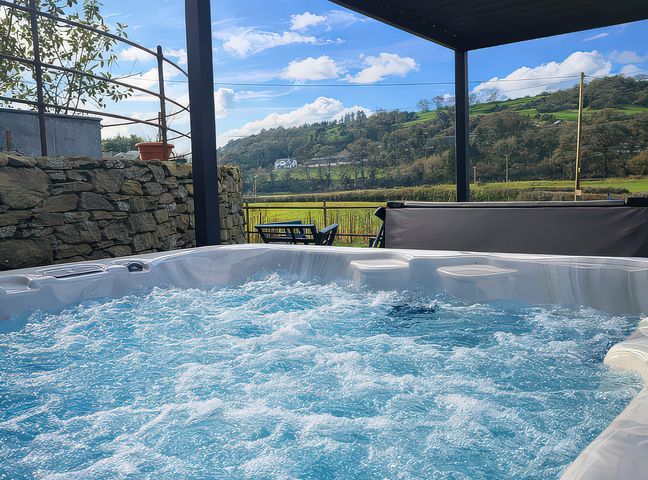 A hot tub and outdoor seating at The Old Cartshed | Yr Hen Gwt Cart in Llangernyw