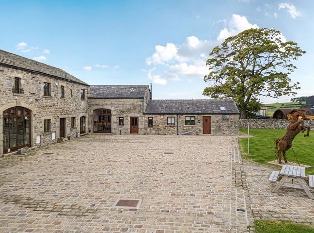 An outdoor area with stone buildings and a tree at Orcaber Farm Barn in Lancaster