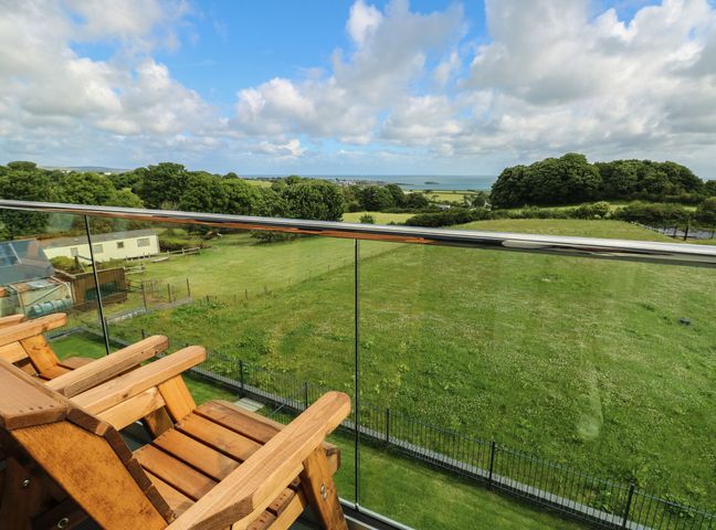 A balcony with deck chairs overlooking a green field and sea at Glynllifon 9 Marian-glas near Benllech