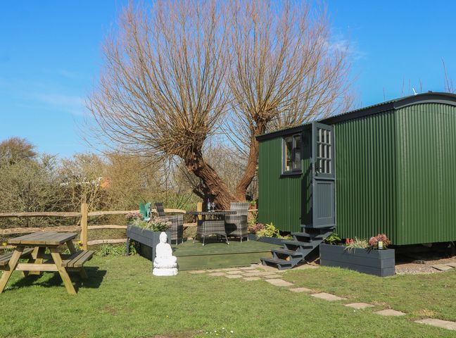 A garden with a shepherd's hut, table, chairs, and a tree at Salt Haven Shepards Hut Pevensey