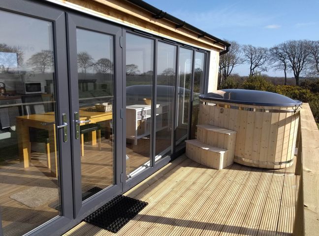 A deck with a hot tub and outdoor seating at Cleeves Cabins 2, Arran Luxury Lodge with hot tub in St. John's Town Of Dalry