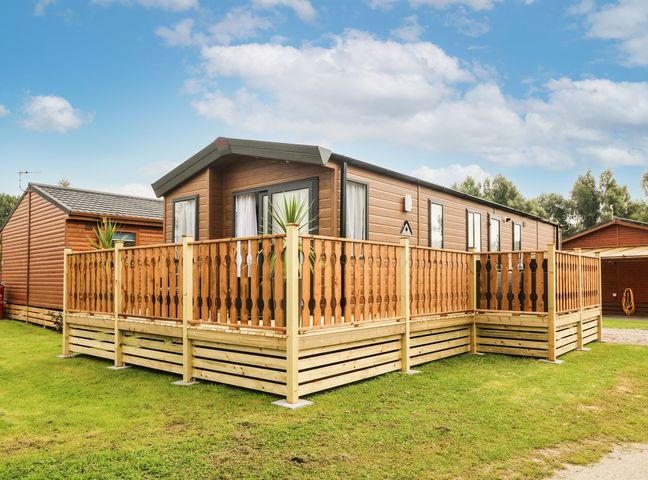 A caravan with a wooden deck at Hedgehog Lodge in Carnforth