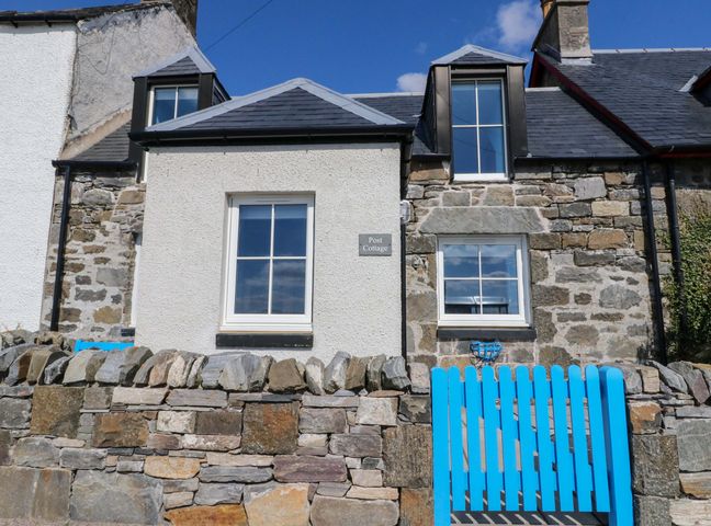 A house with a stone wall and blue gate at Post Cottage in Arisaig