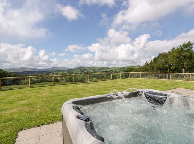 A hot tub on grass with hills and blue sky at Yr Onnen