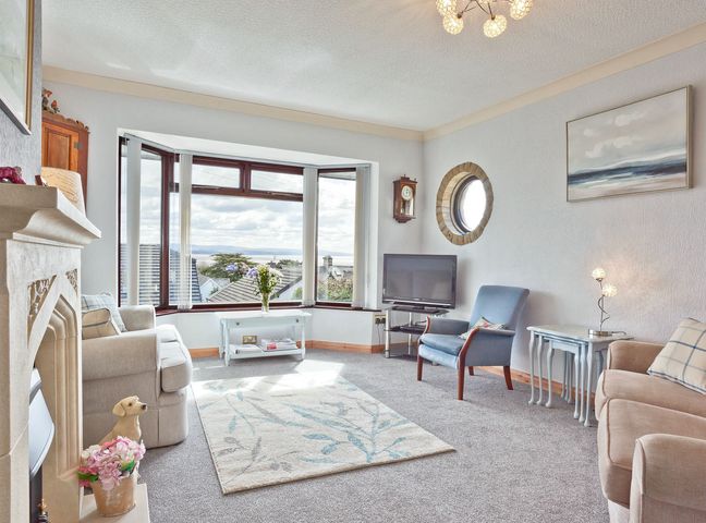 A living room with a sofa and armchair by a bay window at Lothlorien in Grange over Sands