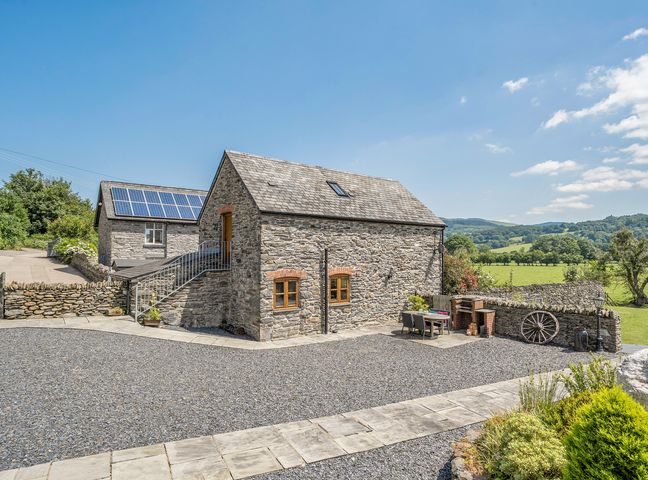 A stone house with a gravel driveway and solar panels at The Granary in Corwen