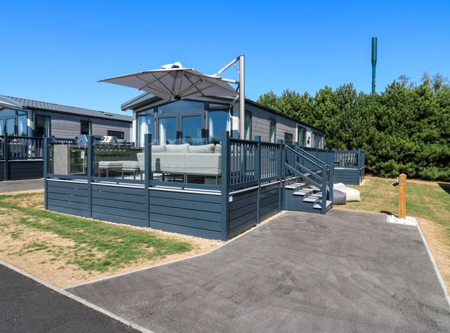 A deck with a couch and umbrella at Lakewood Plot 3 St. Osyth