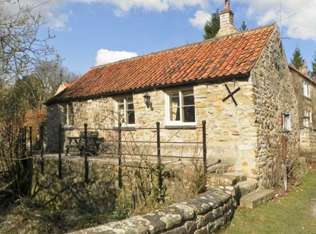 A stone cottage with a tiled roof and metal railing in a rural setting at Beckside in Lastingham