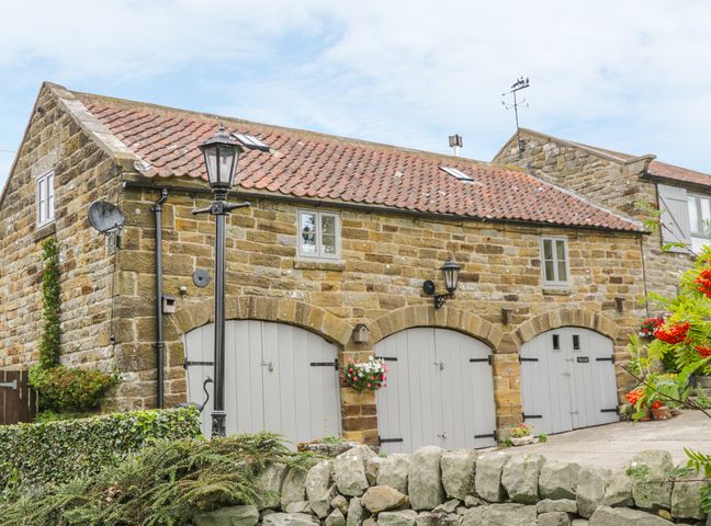 A stone building with three arched gray doors and a tiled roof with windows at The Loft in Staintondale