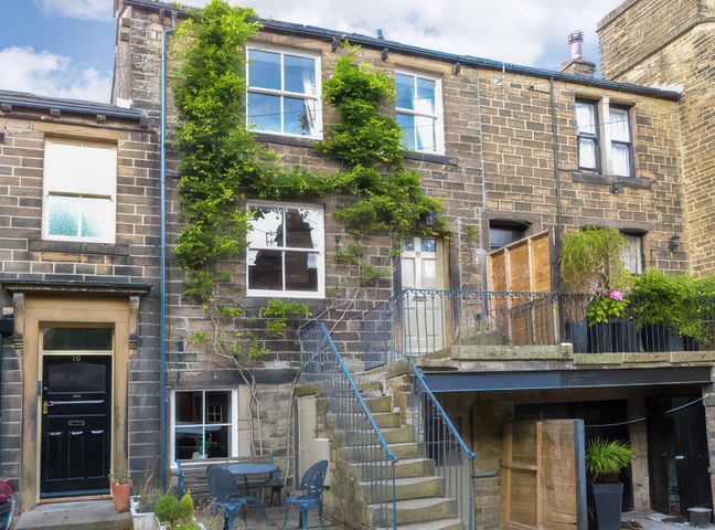Exterior of a stone building with multiple windows a black door stairs leading to a raised door and patio with plants at The Old Forge in Haworth