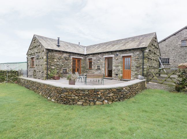 A stone cottage with wooden doors and windows a stone patio with benches and green grass at Little Crake Howe in Selside near Kendal