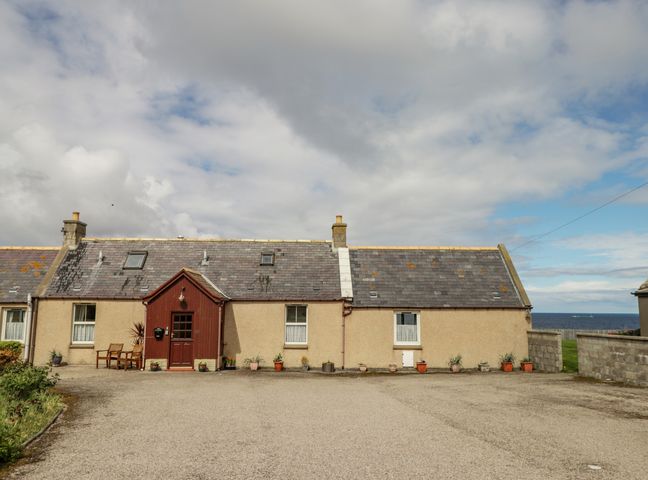 A row of connected houses with a red door and potted plants on a driveway at Braehead Croft in Portessie near Buckie