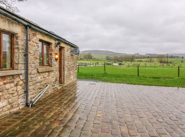 A stone building with windows and a door next to a cobblestone driveway and a grassy field at Orcaber Farm Retreat in Austwick
