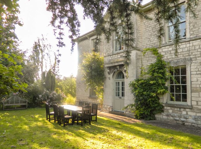 A stone house with windows and a door with outdoor table and chairs on a grassy lawn surrounded by trees at Old Station Farm Amotherby Malton