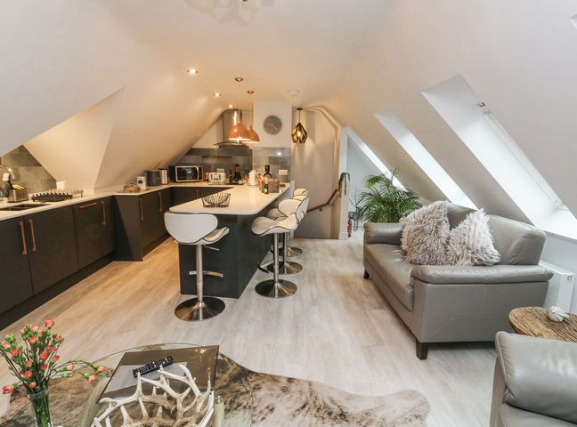 An open plan kitchen and living area with bar stools at a kitchen island and leather sofas at Treetops in Southerton