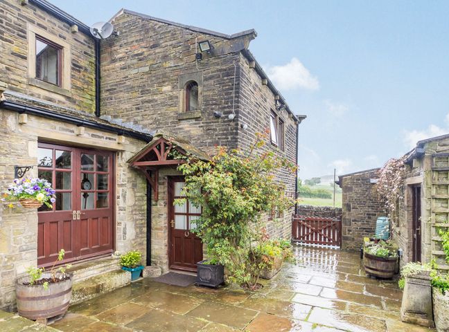 An outdoor stone patio area with wooden doors plants and a gate at Green Clough Farm in Haworth