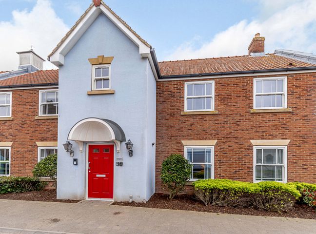 Front of a building with blue and brick walls red door and windows with shrubs at Sunrise The Bay near Filey