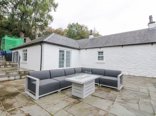 An outdoor patio with gray sectional sofa and a fire pit table at Heatherbank in Garelochhead