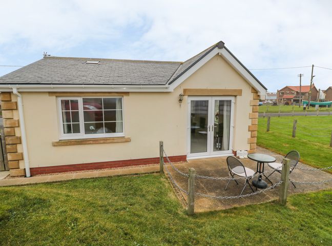A small patio area with a round table and two chairs outside a cream cottage with a pitched roof at White Rock Cottage in Beadnell