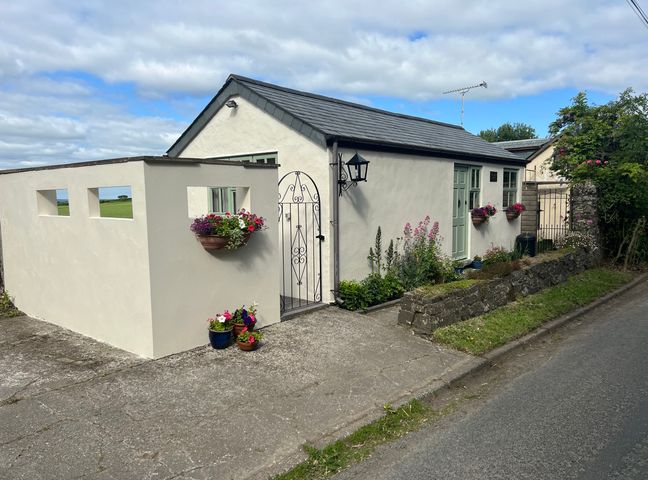 A small white house with a slate roof and flower pots on the walls beside a paved driveway at Palmers Lodge in Egloskerry near Launceston