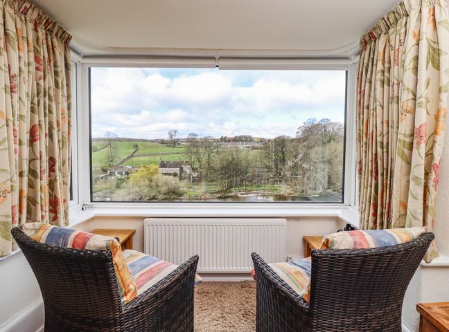 Two wicker chairs with striped cushions facing a large window with floral curtains and a view of countryside at Riverside Grassington Wharfedale