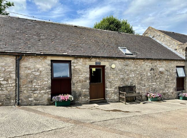 A stone building with a wooden door a bench and flower planters outside at Dover Barn in Parwich near Ashbourne