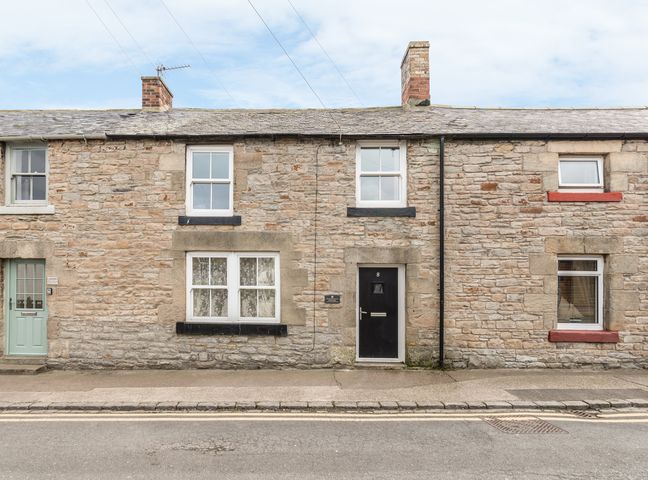 Stone terraced houses with chimneys and various colored doors and windows on a street at Fisherman's Cottage in Seahouses