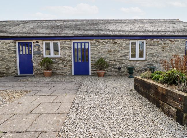 A stone building with blue doors and windows a gravel and paved courtyard with potted plants and a wooden garden bed at Wheal Kitty in St Newlyn East near Newquay
