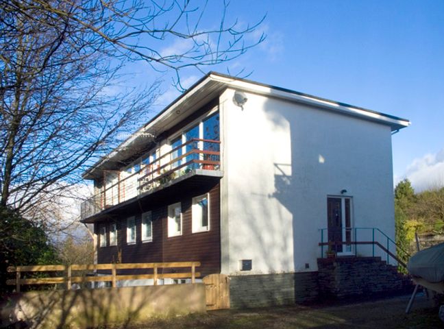 A two-story house with a balcony and a wooden fence surrounded by trees at Park View in Bowness-on-Windermere