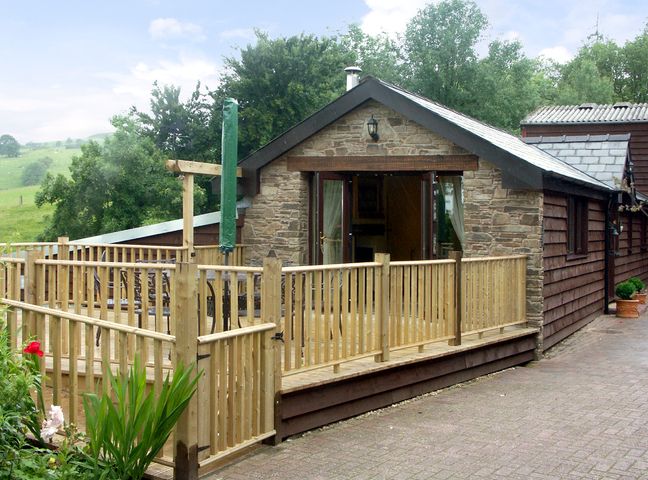 A wooden deck with a table and chairs outside a stone and wood house at Cwm Derw Cottage in Llanafan Fawr near Builth Wells