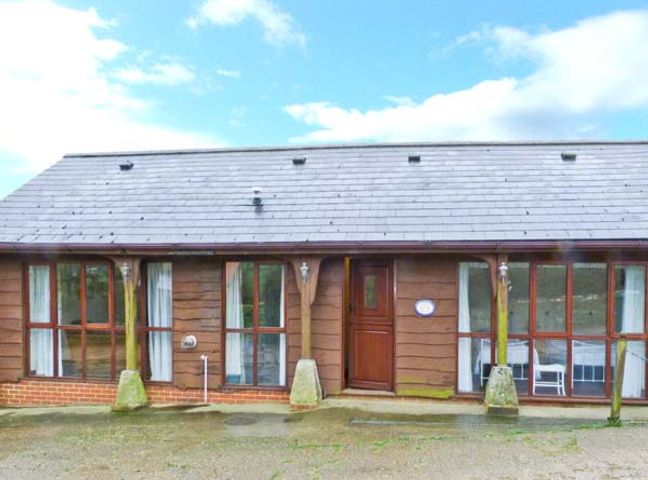 A wooden single storey house with multiple windows and a central door at The Carthouse in Shorwell